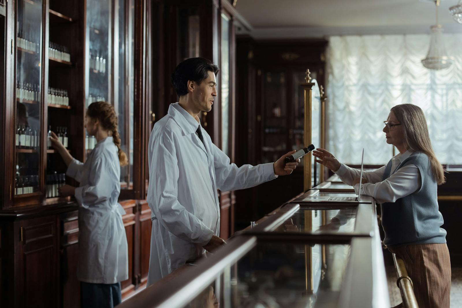 A pharmacist hands medication to a customer at a classic vintage pharmacy counter.