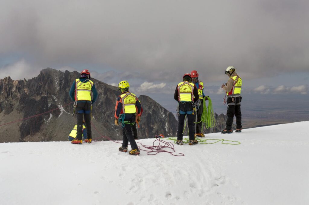 Group of mountain rescuers in safety vests and helmets preparing ropes in snowy terrain.