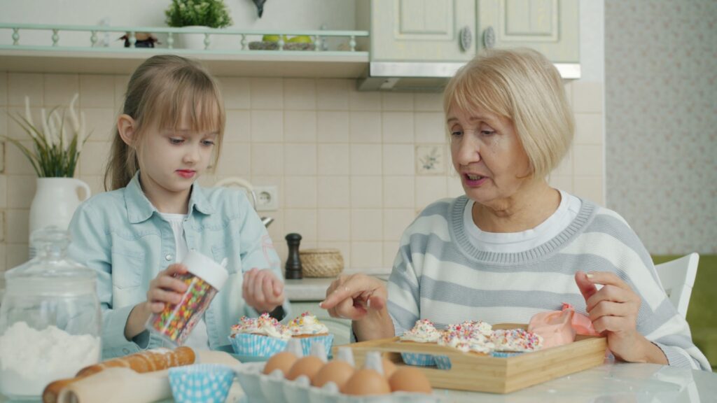 Grandmother and granddaughter decorating cupcakes in kitchen.