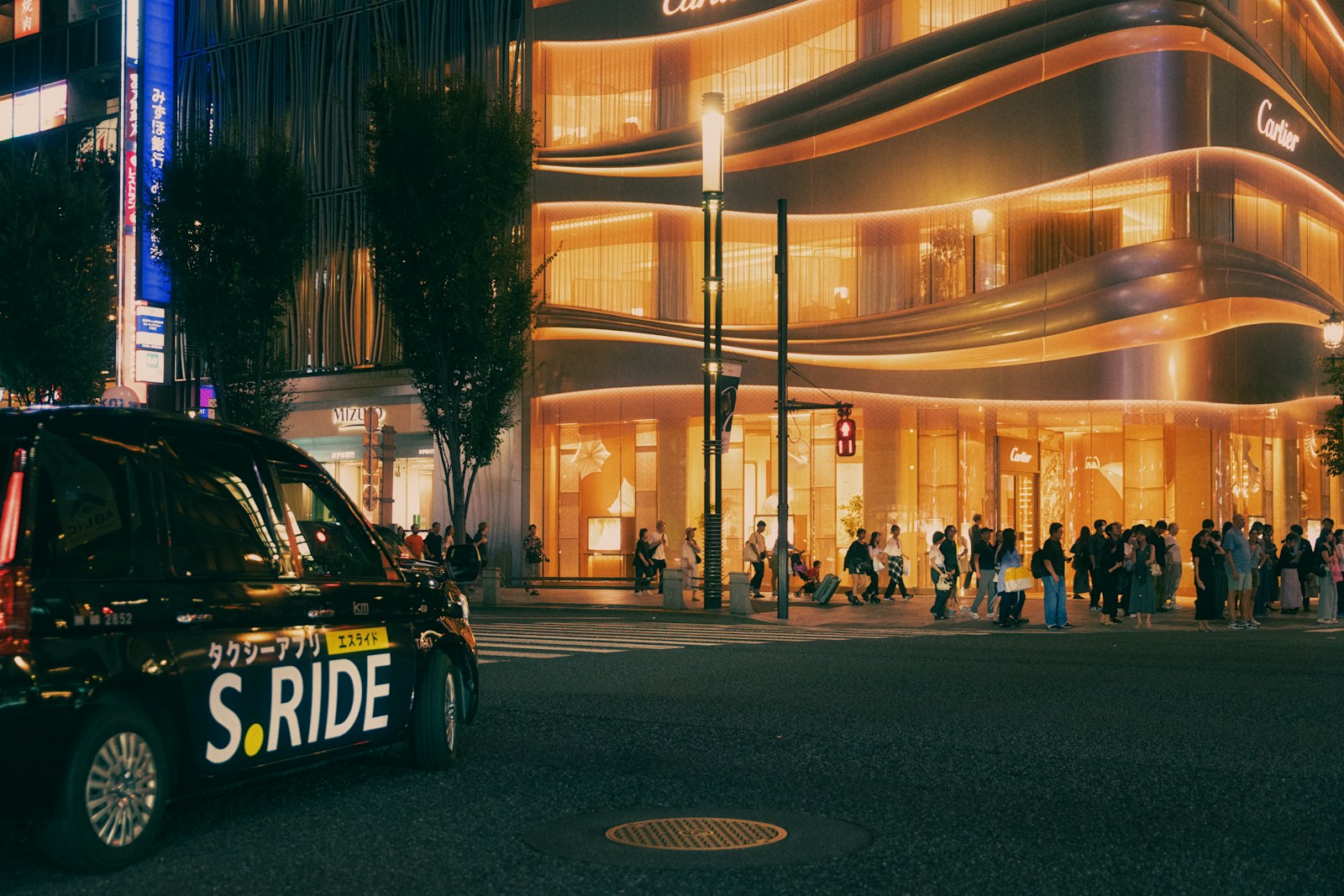 Black taxi with s.ride logo drives past illuminated building