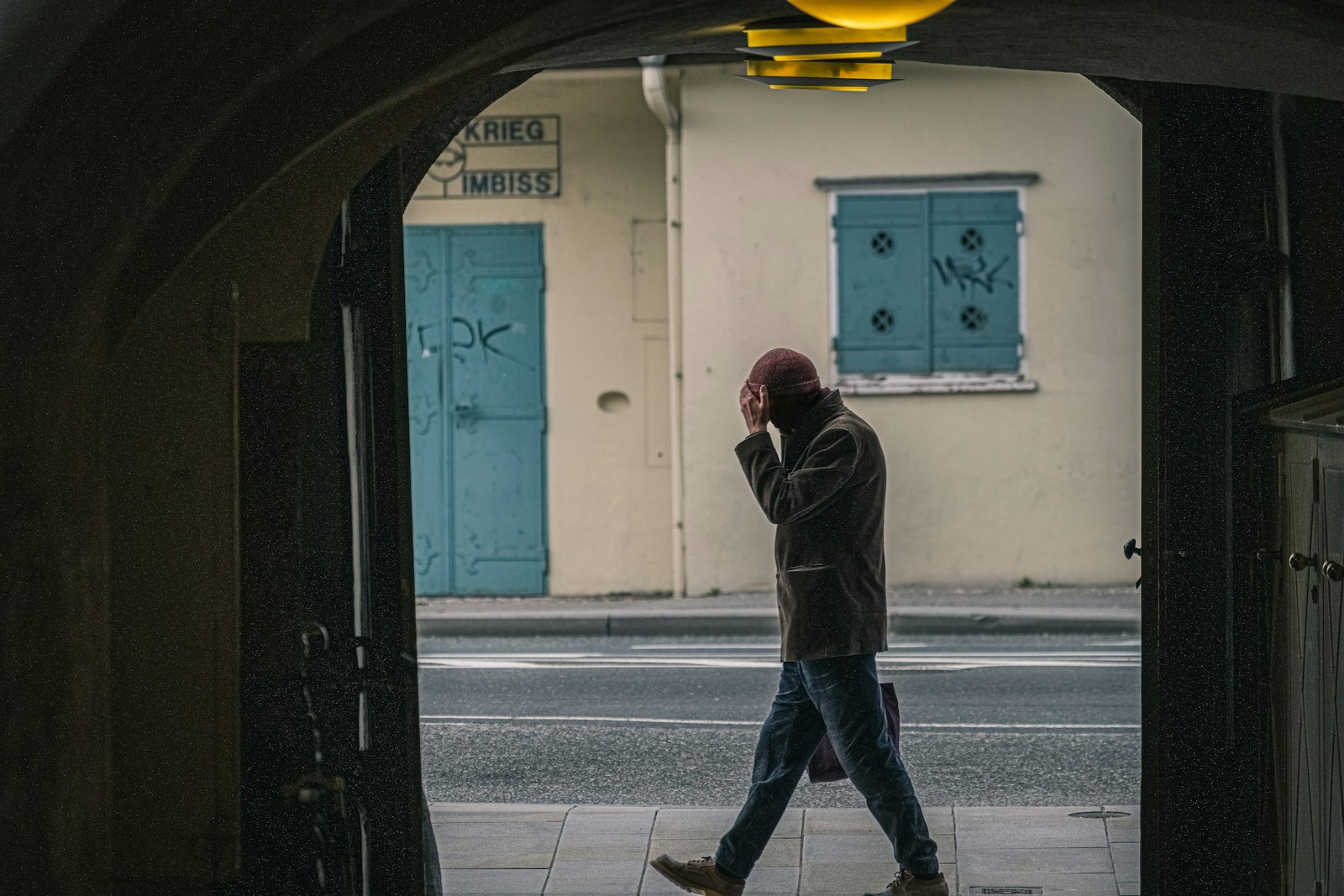 man in black jacket and blue denim jeans standing on sidewalk during daytime