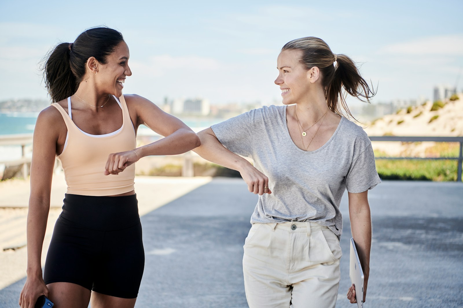 woman in gray shirt elbow bumping with woman in sports outfit