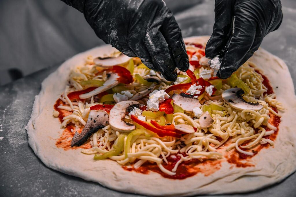 Close-up of hands adding toppings to pizza dough with cheese and vegetables.