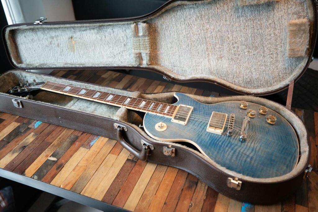 Close-up of a blue electric guitar in an open case on a wooden table, indoors.