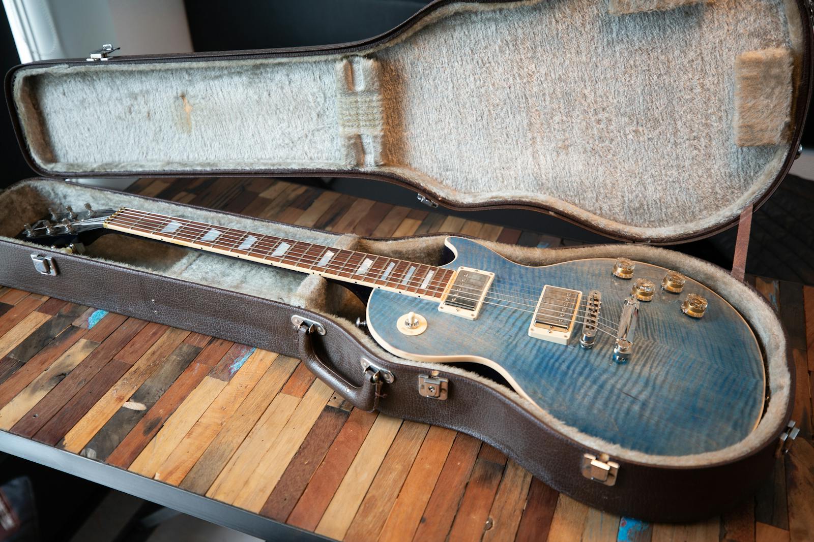 Close-up of a blue electric guitar in an open case on a wooden table, indoors.