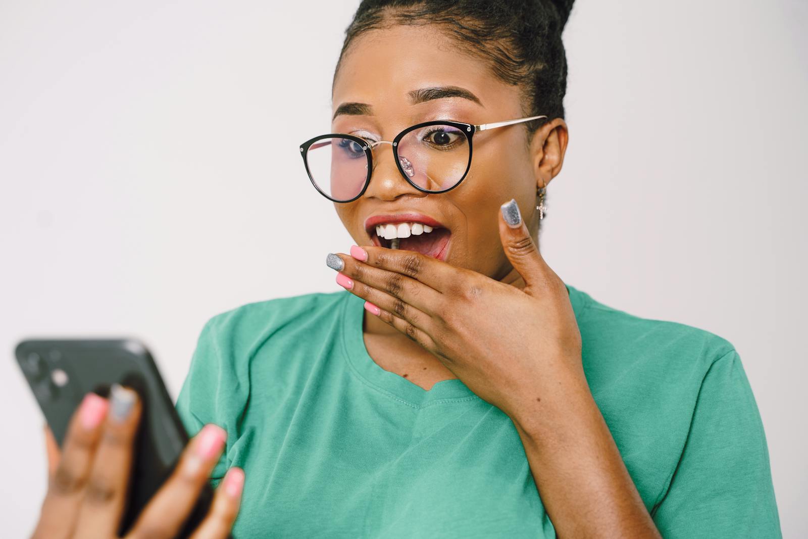 A young woman in glasses looks surprised while using her smartphone indoors.