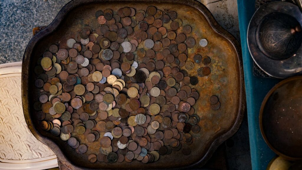 A rustic tray filled with various vintage coins, showcasing rich metallic textures and patterns.