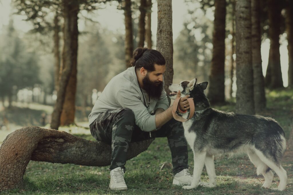 man in gray jacket and blue denim jeans sitting on tree log with white and black