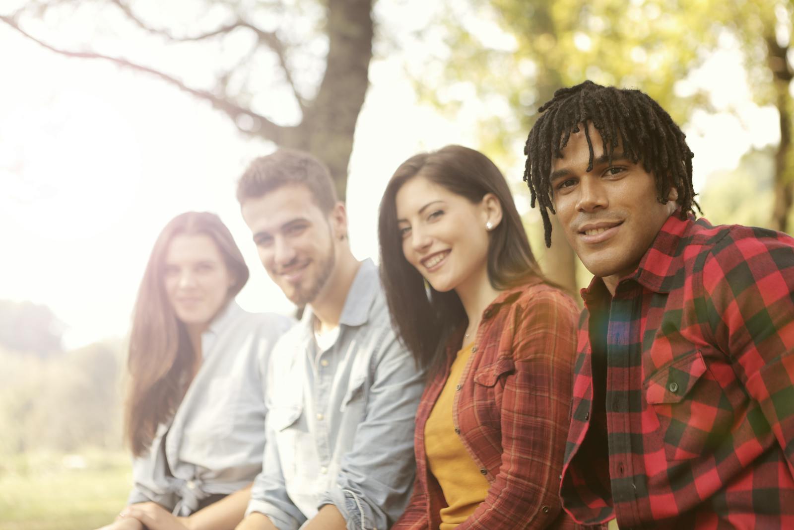 A diverse group of friends sitting outdoors, smiling and enjoying a sunny day.