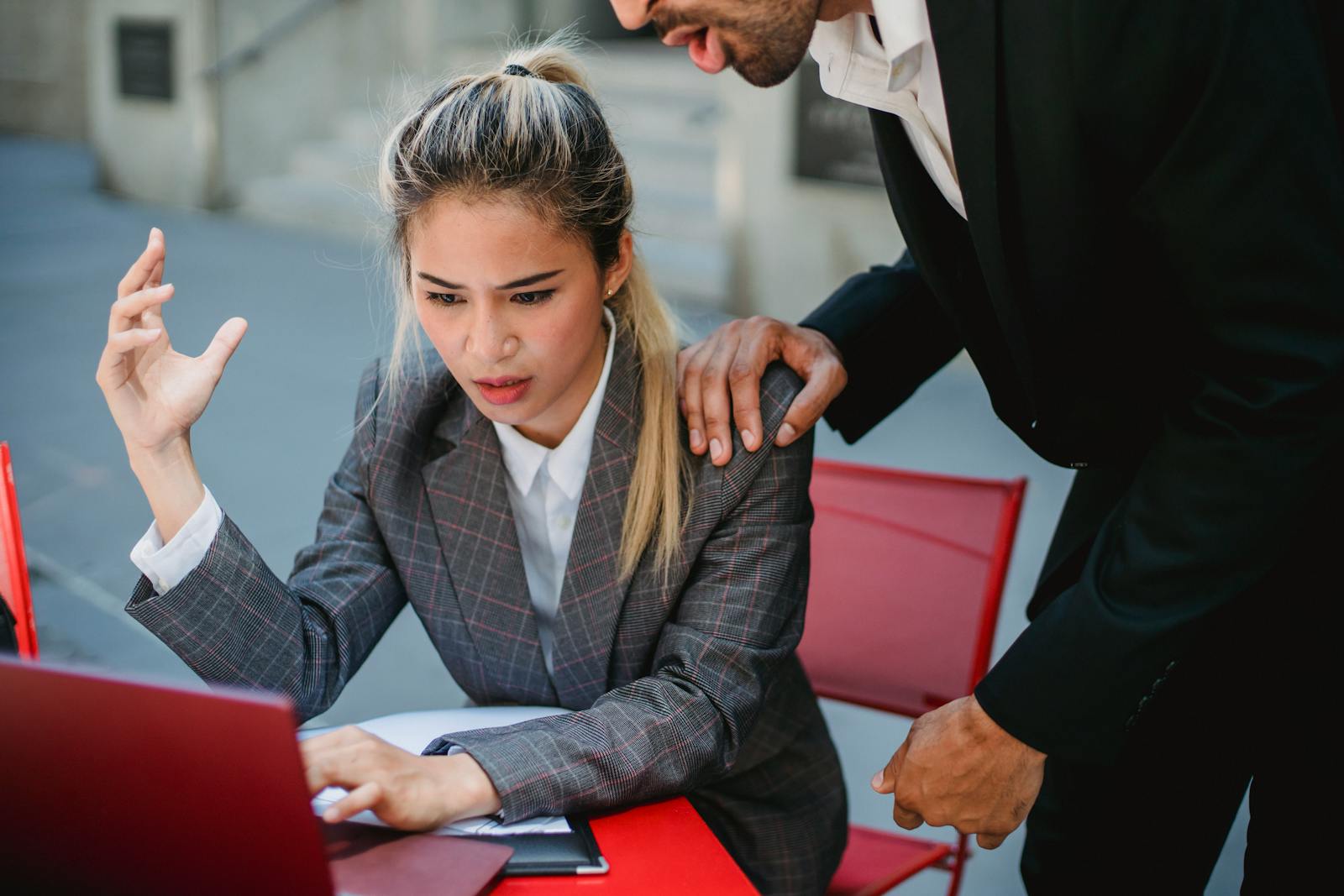 Two professionals engaged in an intense discussion outdoors using a laptop.
