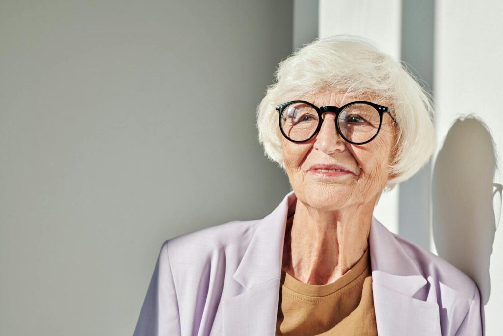 Close-up of a stylish senior woman with glasses in soft light.