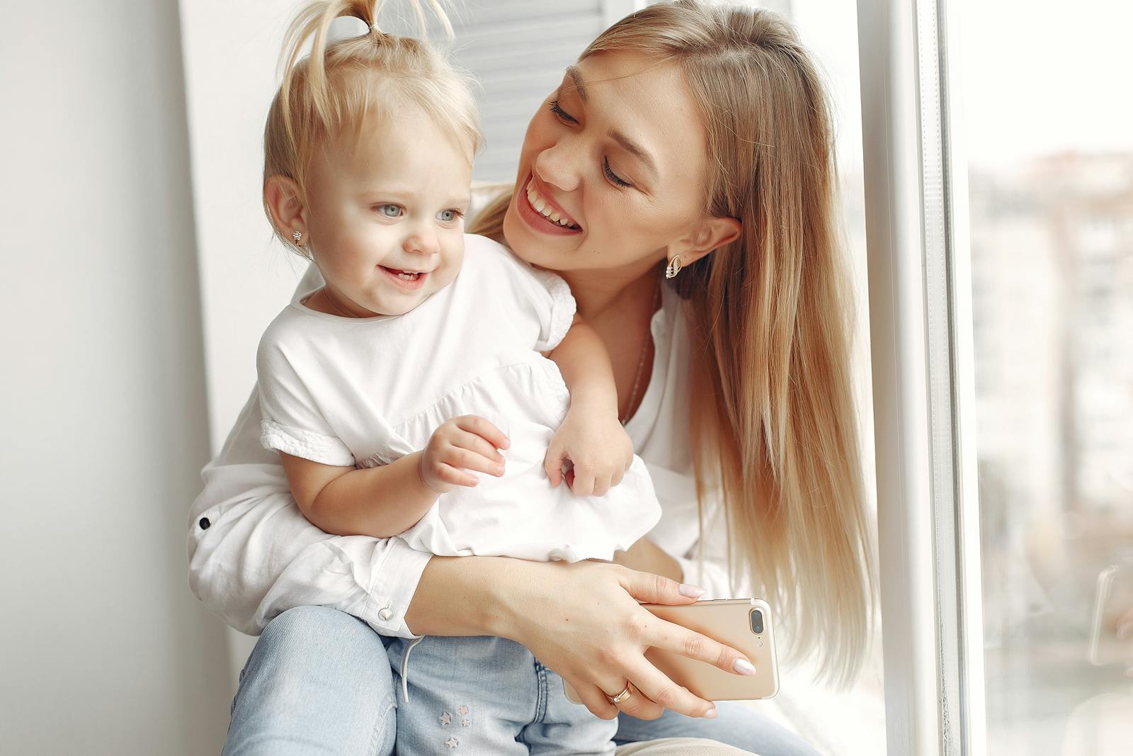 Mother and daughter bonding with smiles while sitting by the window, showcasing love and happiness.