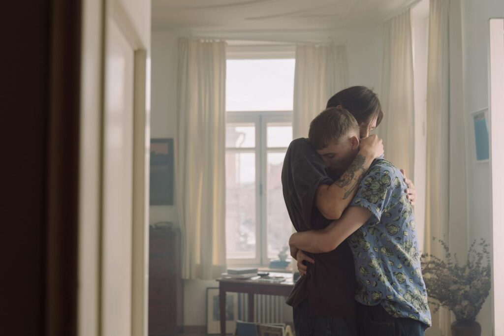 A loving embrace between two men in a softly lit room, showcasing warmth and affection.
