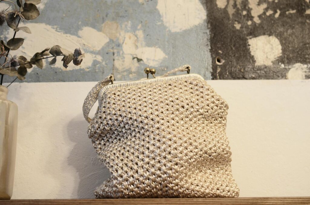 Organic knitted handbag with ornament and metal fastener on desk near rough wall in house