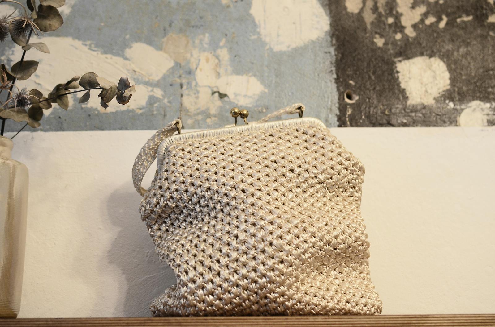 Organic knitted handbag with ornament and metal fastener on desk near rough wall in house