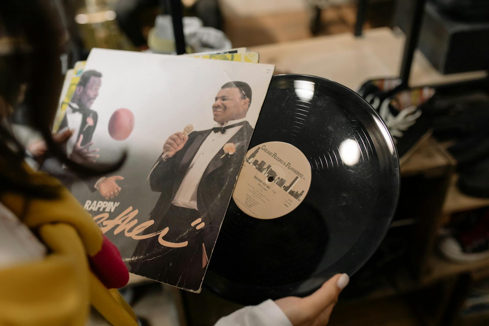 Close-up of a vintage vinyl record and album cover being held by a person indoors.