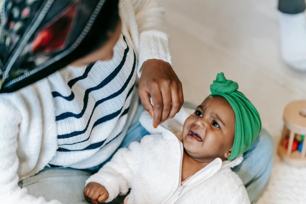 An adorable baby wearing a green turban interacts with mother indoors, showcasing a tender family moment.