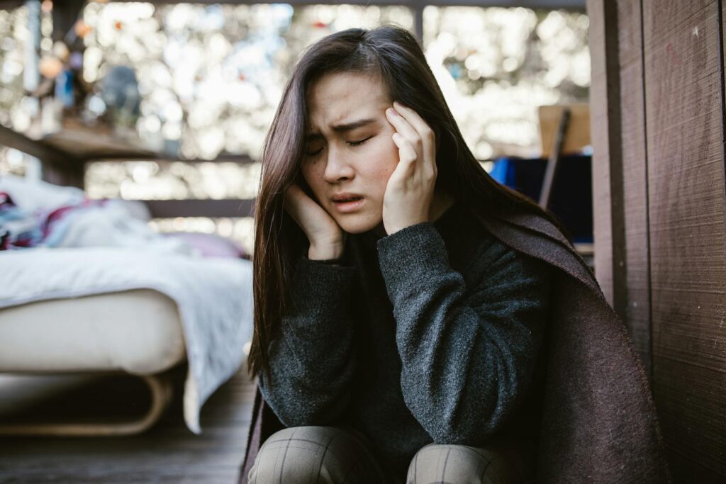 A young woman holds her head in distress while sitting indoors, capturing an emotional moment.