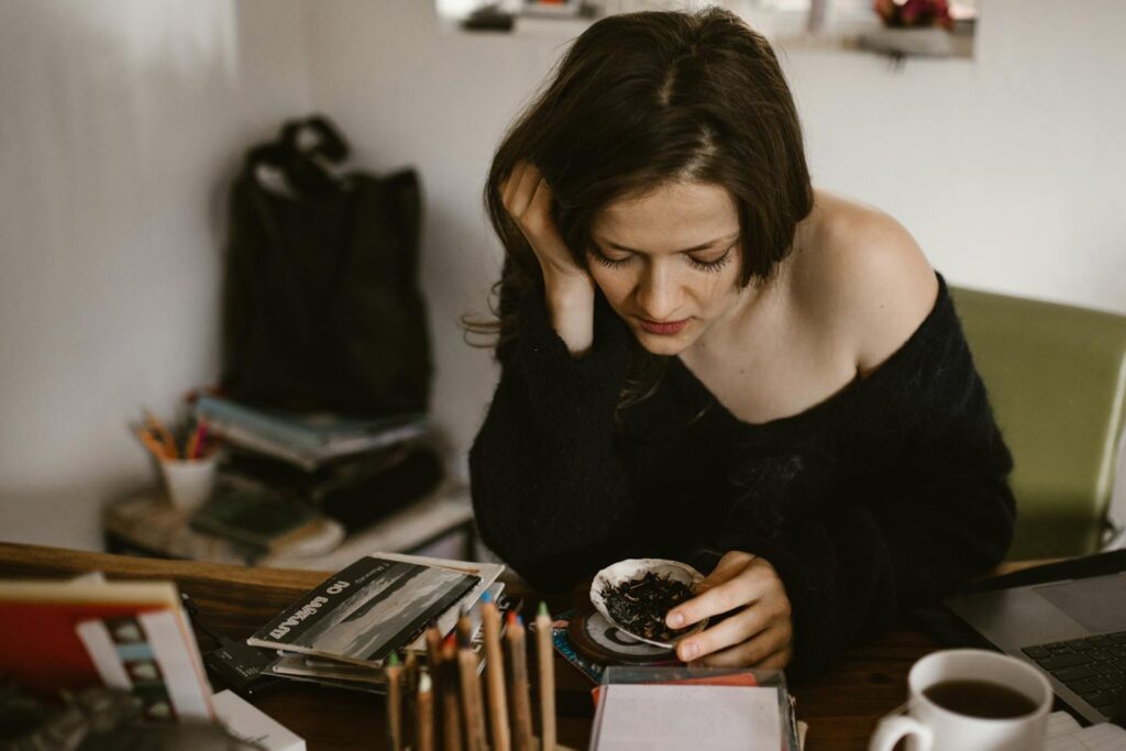 A woman deeply engaged in thought, sitting indoors with coffee and scattered books.
