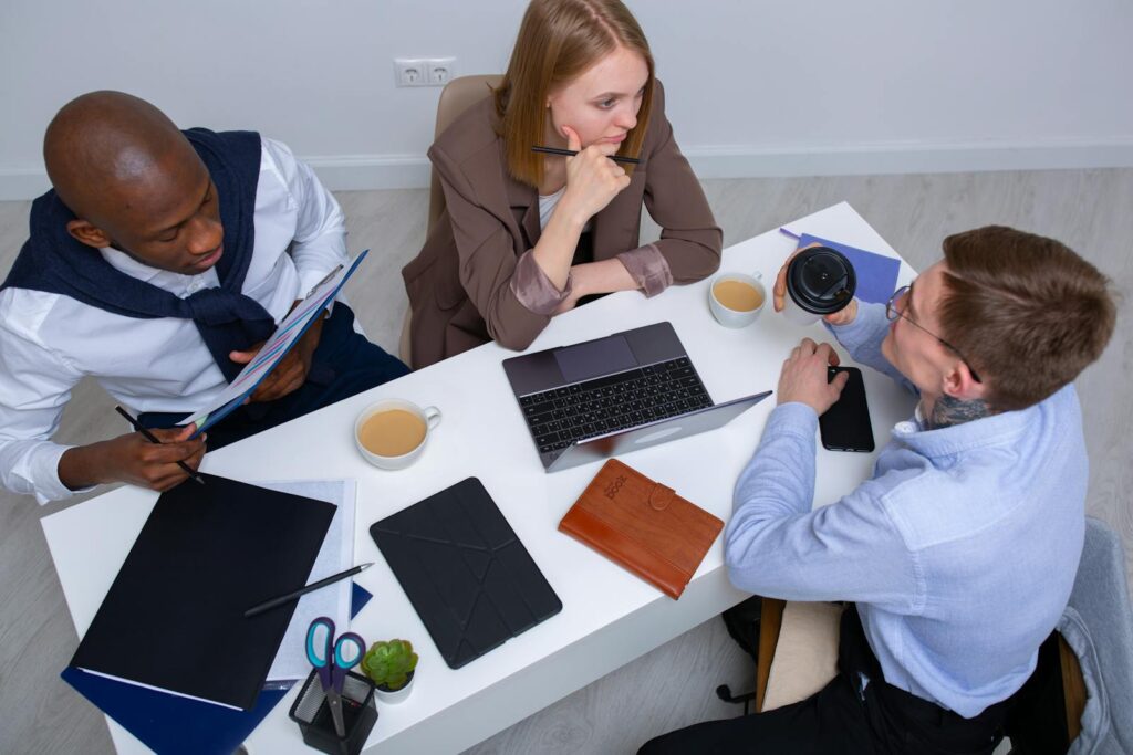 Diverse colleagues engaged in discussion around a conference table with technology and notes.