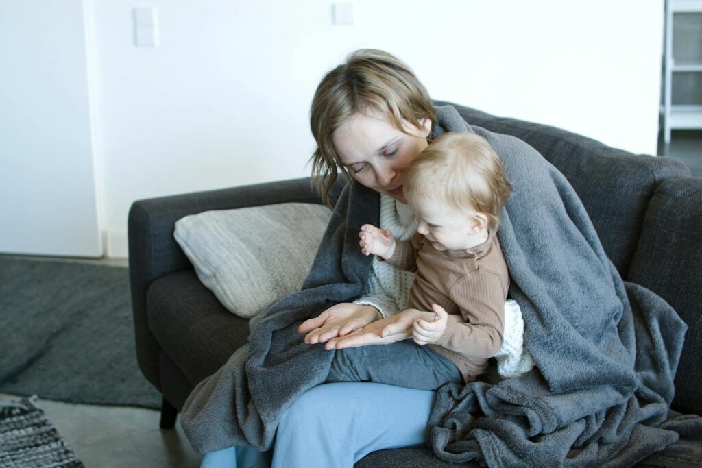 A mother and her baby bonding on a cozy sofa under a blanket, showcasing warm family moments.