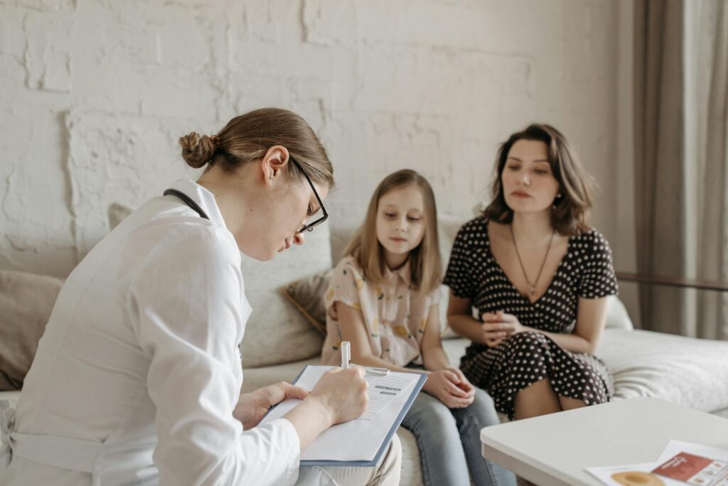 A female doctor consults with a mother and daughter inside a cozy room.