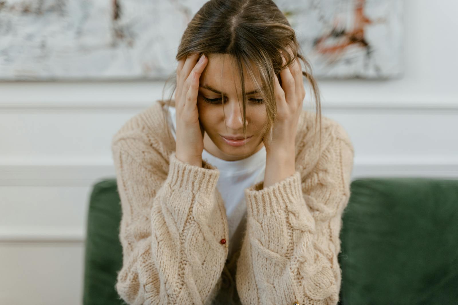 A woman sitting on a sofa holding her head, expressing stress and frustration indoors.