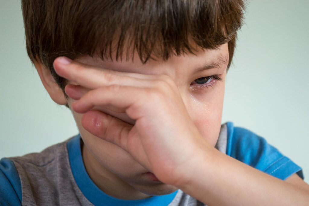 Close-up portrait of a young boy wiping away tears, expressing emotion.