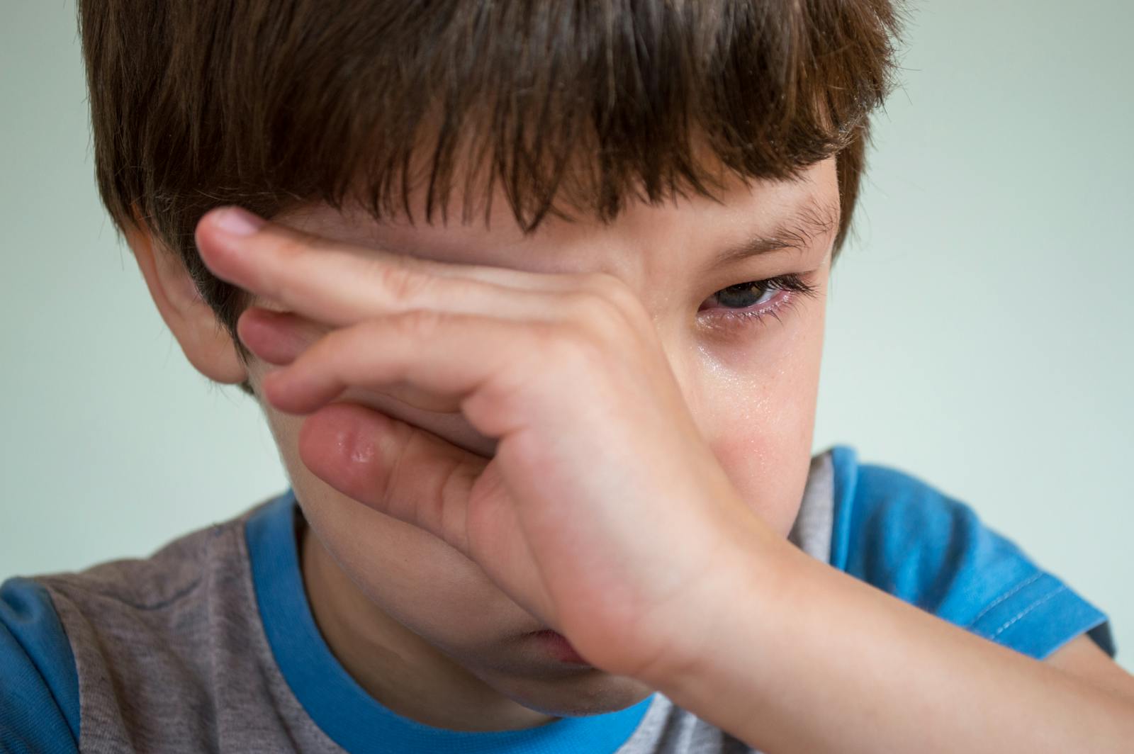 Close-up portrait of a young boy wiping away tears, expressing emotion.