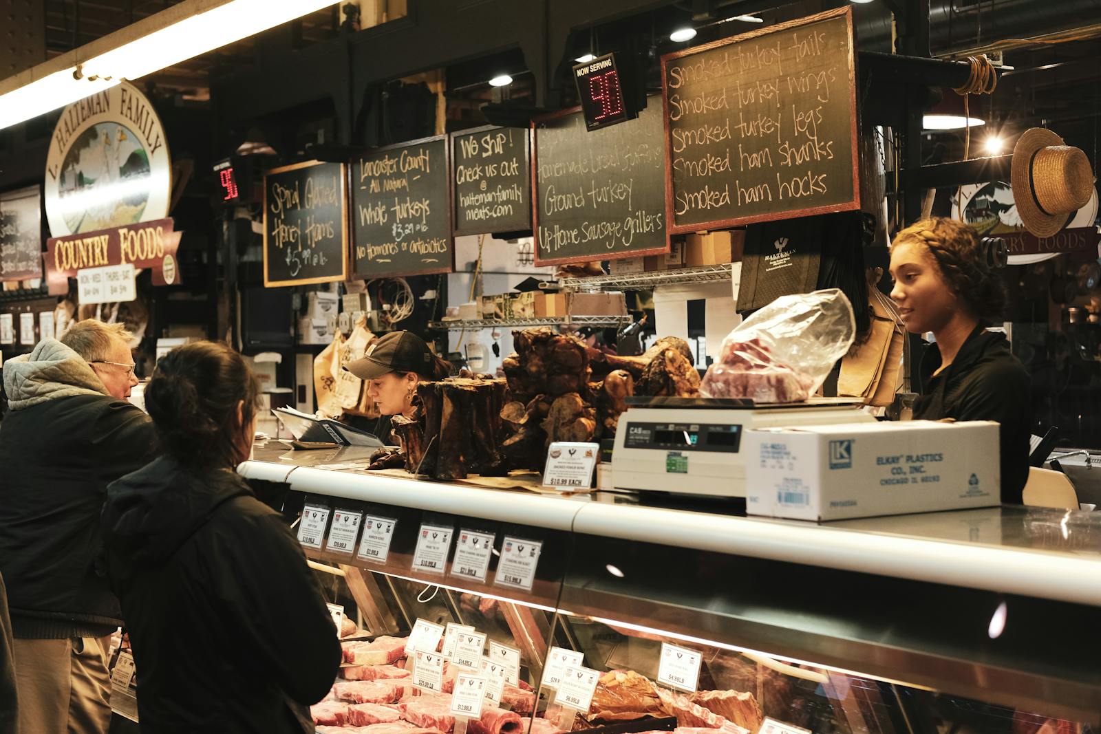 A bustling meat shop showcasing various meats with employees serving customers over a counter.