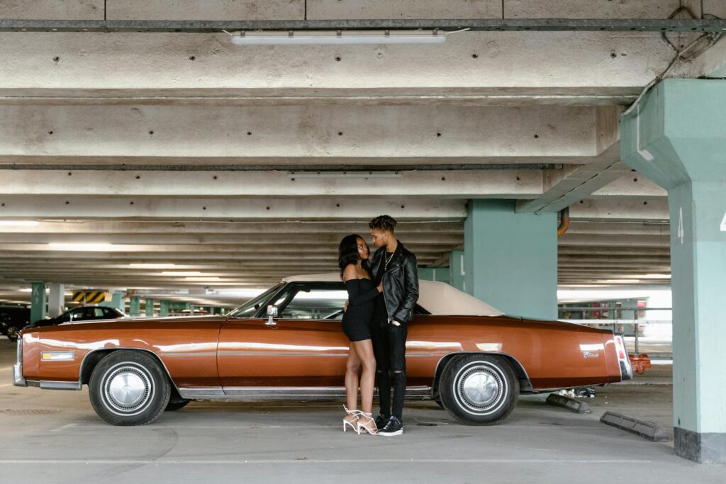 Couple standing near a classic brown Cadillac in a parking garage, sharing a romantic moment.