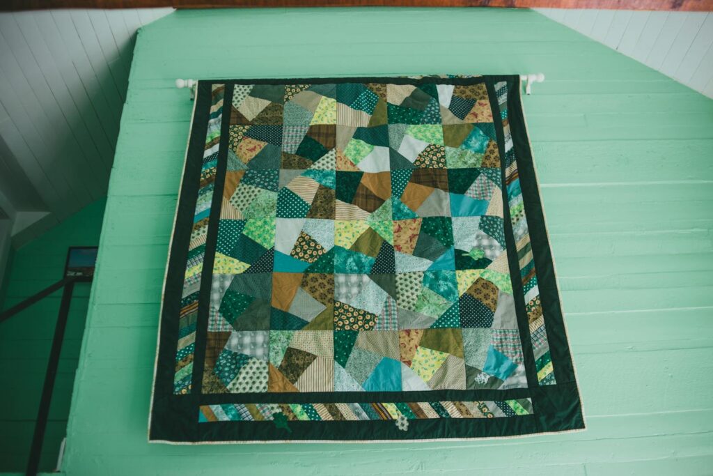Vibrant patchwork quilt with a geometric design hanging on a mint green wall indoors.