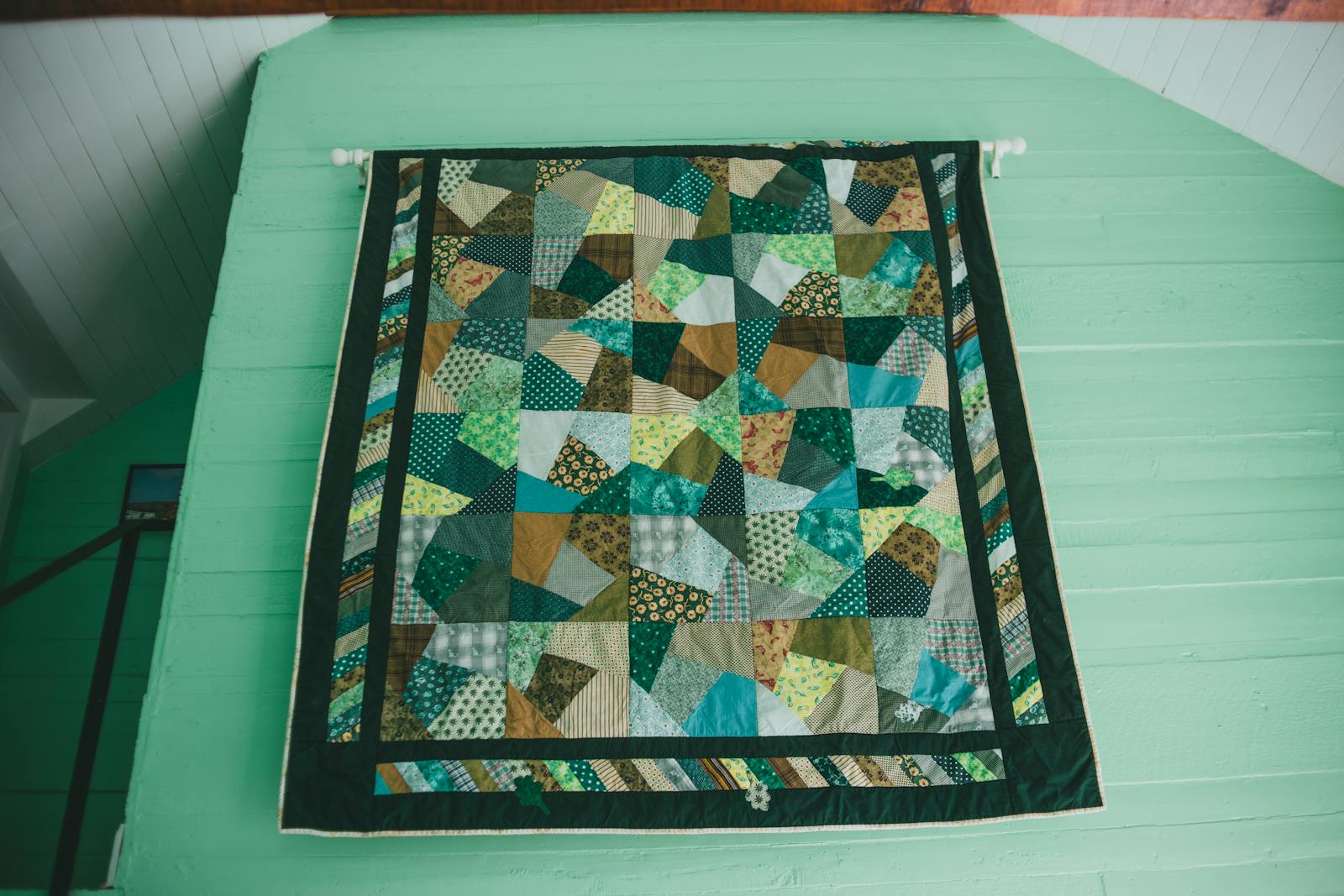 Vibrant patchwork quilt with a geometric design hanging on a mint green wall indoors.