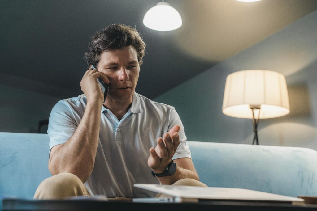 Man speaking on a smartphone while sitting on a sofa, working from home.