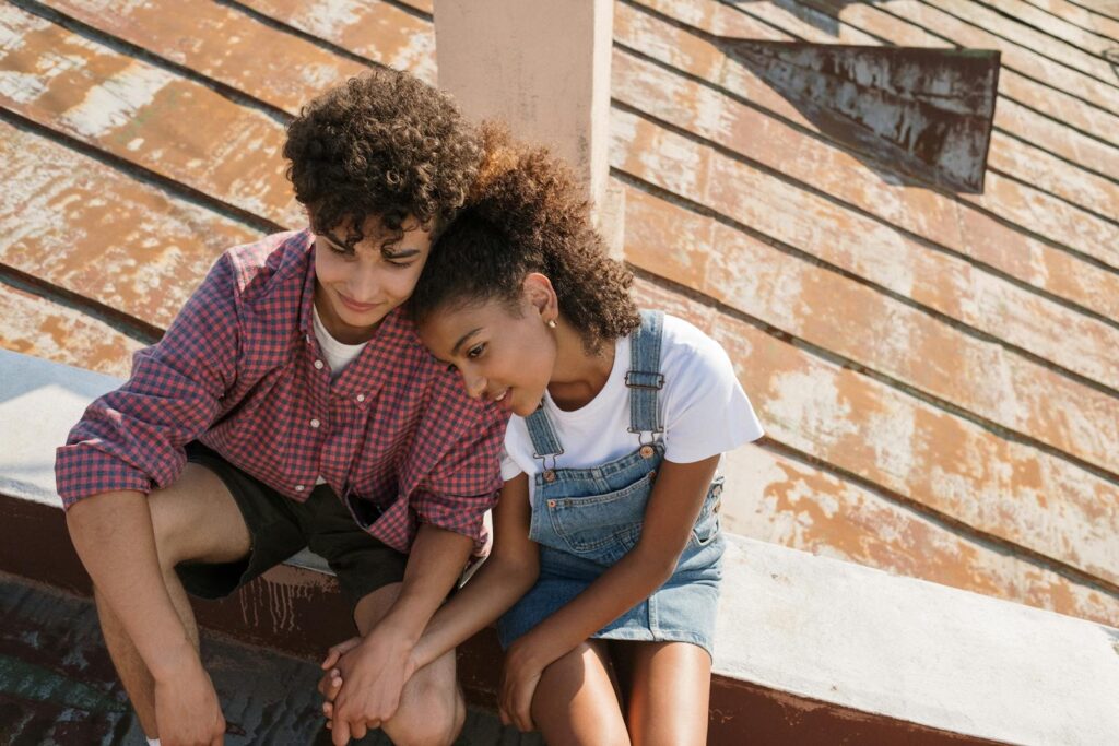 Teen couple sitting close on a sunny rooftop, sharing a tender moment.