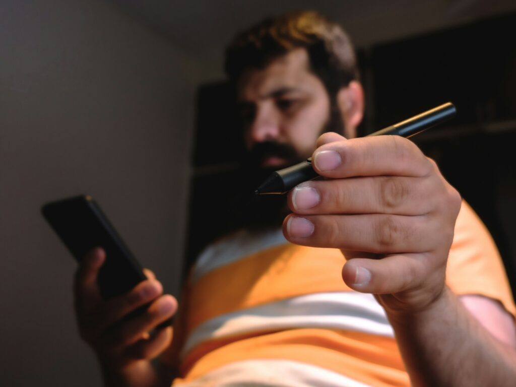 man in orange and white stripe shirt holding black smartphone