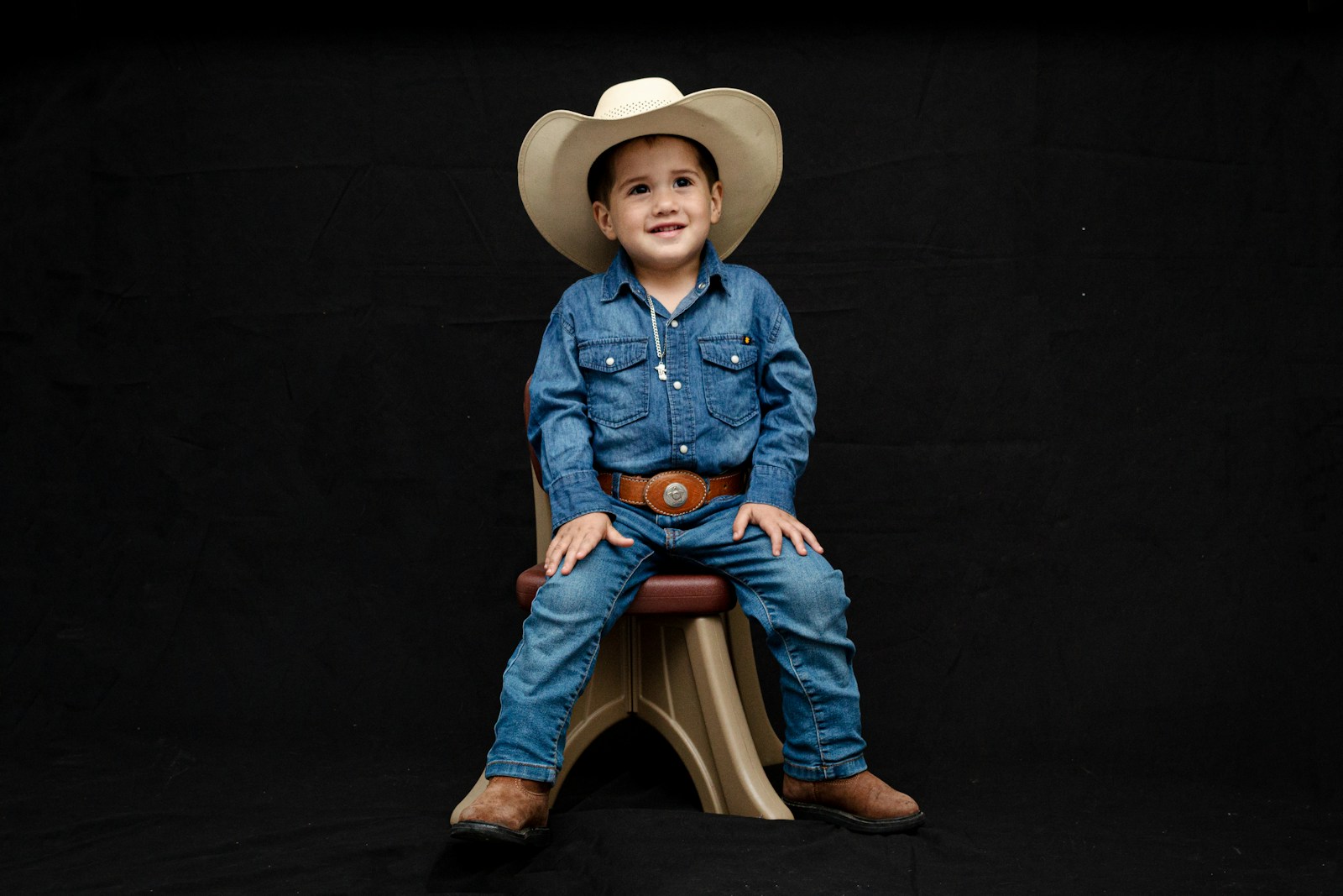 a young boy wearing a cowboy hat sitting on a stool