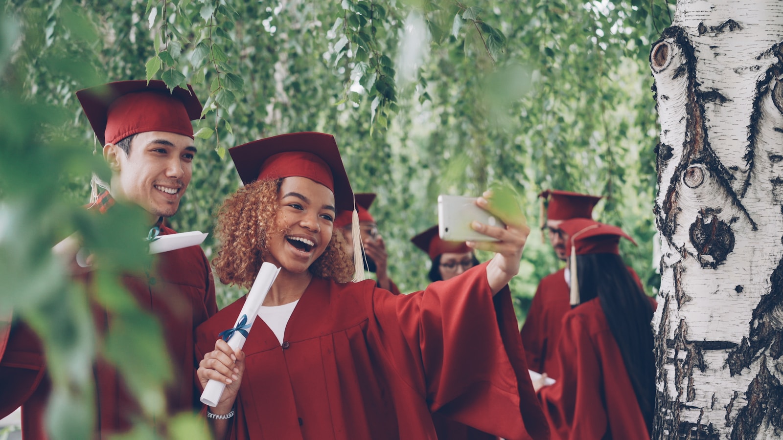 Graduates in red gowns take a selfie with diplomas.