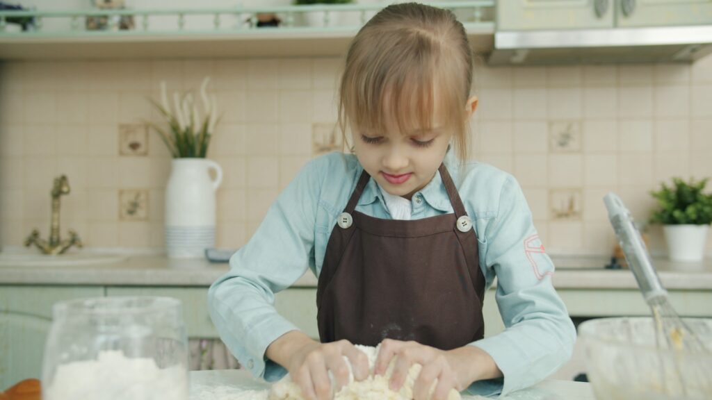 Young girl wearing apron kneading dough in kitchen.