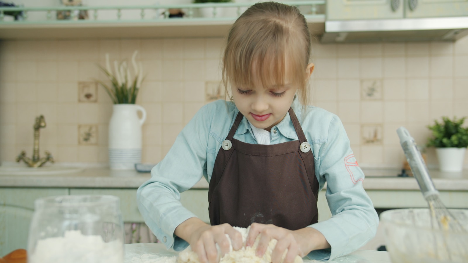 Young girl wearing apron kneading dough in kitchen.
