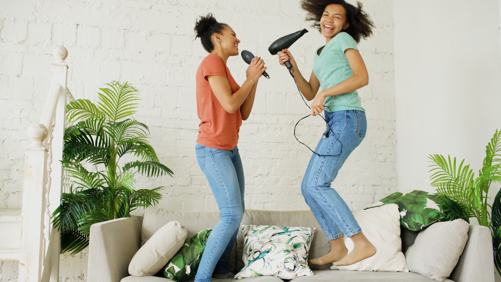 Two young women jumping on a couch singing