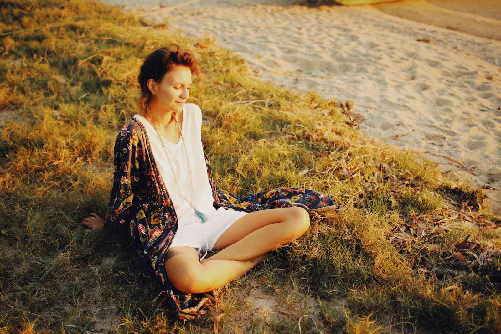 a woman sitting in the grass on the beach