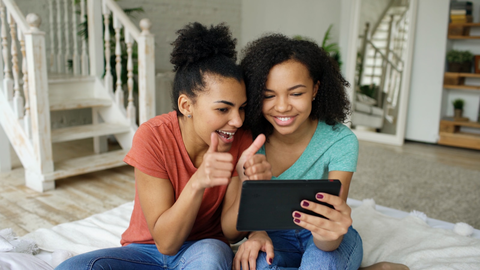 Two women smiling and giving thumbs up with tablet.