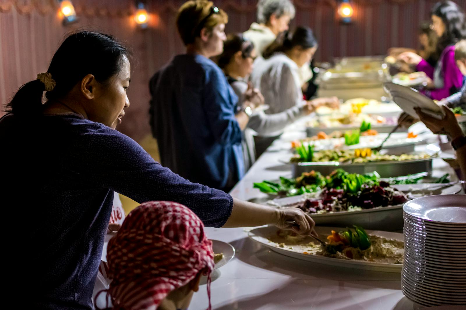 A diverse group of people enjoying a buffet dinner indoors with various dishes.
