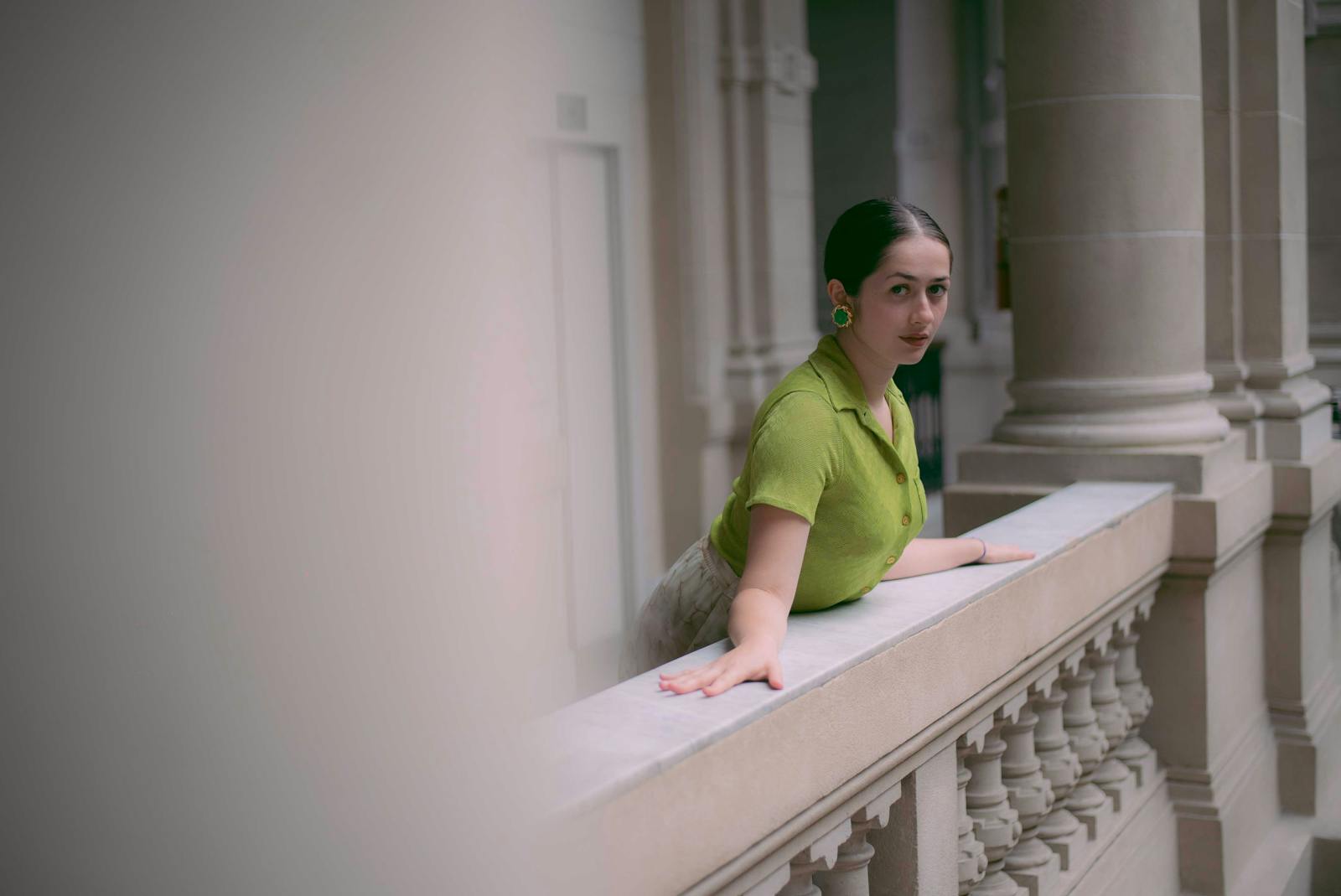 Elegant fashion portrait of a woman in a green blouse leaning on an ornate balcony.