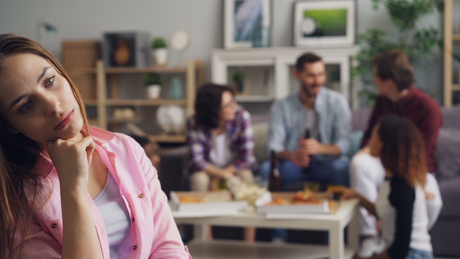 A young woman looks lonely at a party while others engage in conversation.