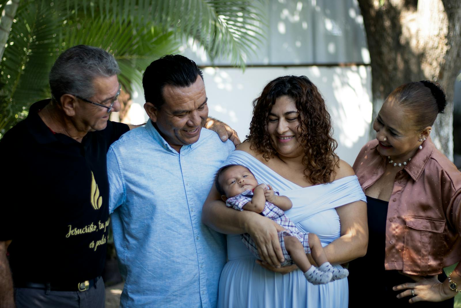 Joyful family gathering with proud parents and grandparents holding a newborn baby outdoors.