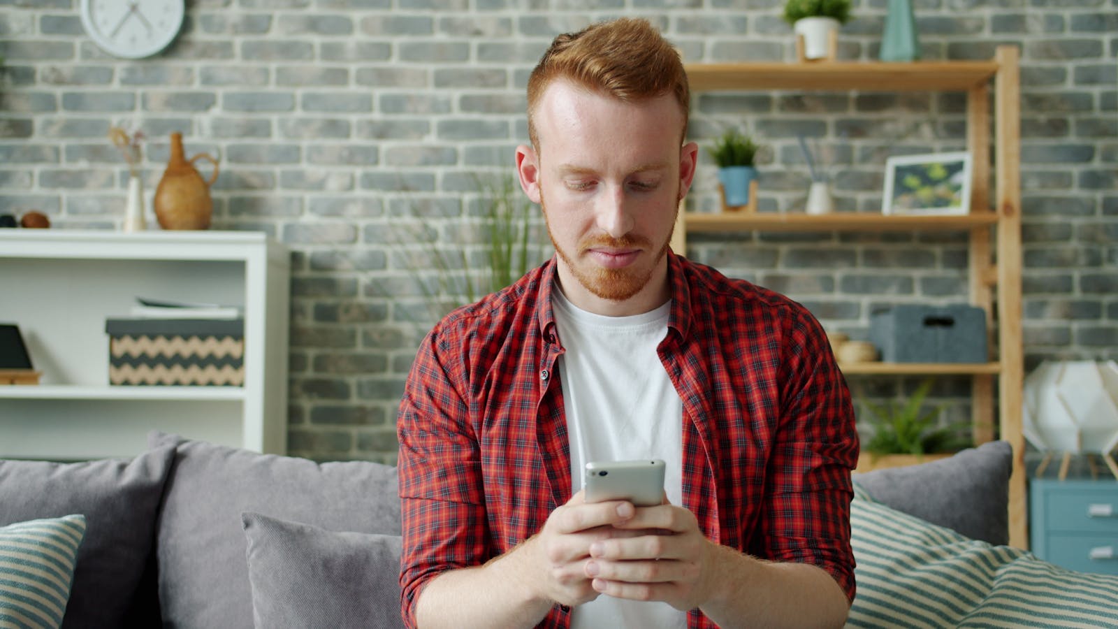 Man in red plaid shirt texting on smartphone at home, modern lifestyle.