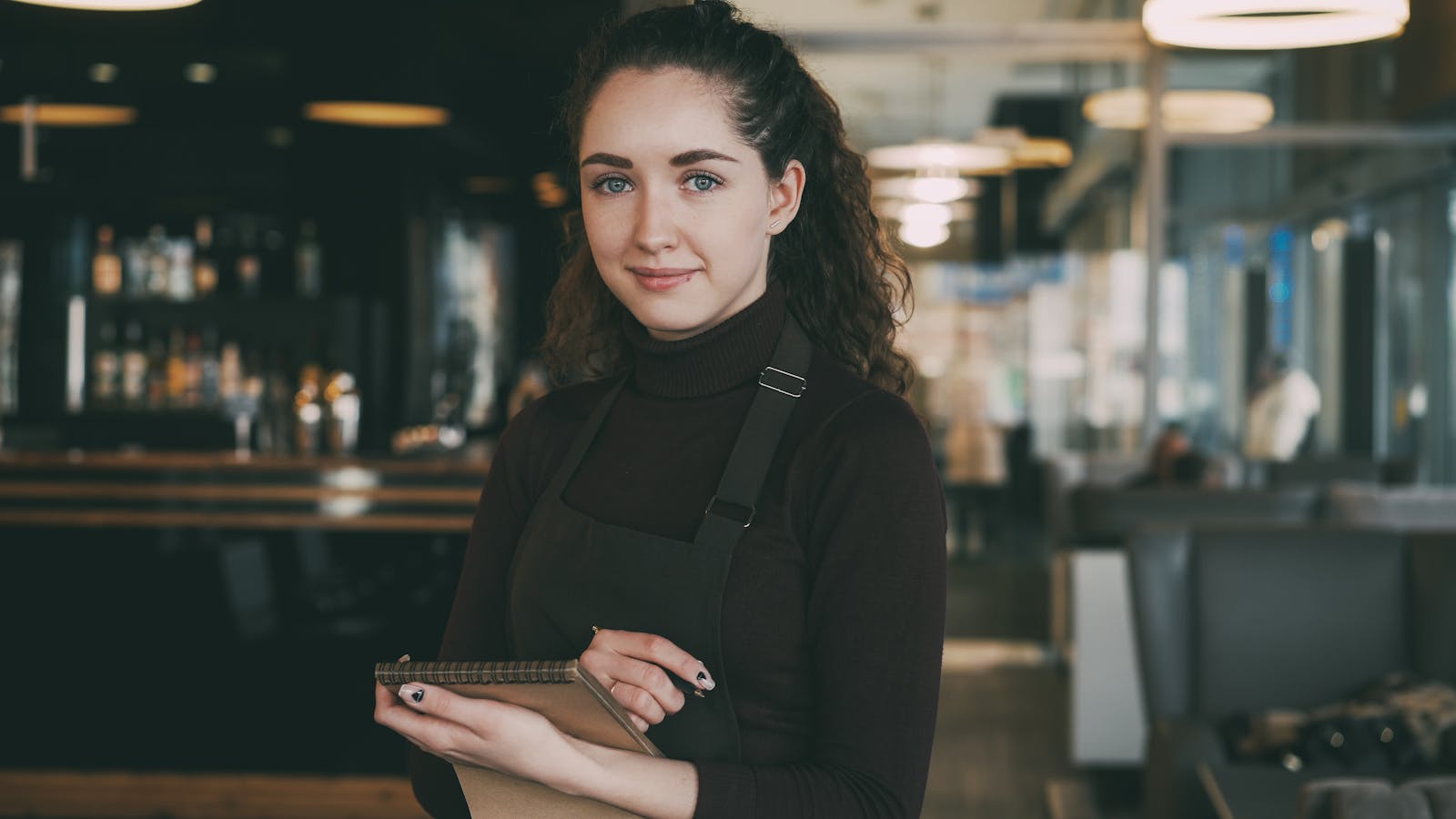Friendly waitress holding a notepad, ready to take orders in a modern cafe setting.