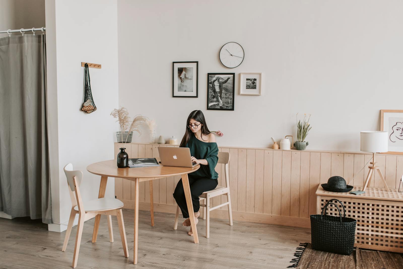 Full length of focused barefoot female in eyeglasses and casual clothes with open shoulder typing on laptop keyboard while sitting at table in spacious living room
